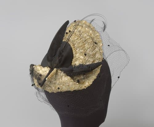 Hoed met bol in platte pannenkoekvorm, met voile met nopjes en rechts op de hoed een piek als een vliegende vogel van veren by Marie Arnouts