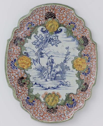 Plaat, ovaal met uitgeschulpte rand met herdersscène in blauw, omlijst door een veelkleurige bloemenrand by anonymous