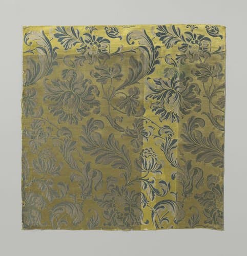 Fragment gele zijdesatijn met patroon in wit en blauw, bestaande uit twijgen met gekruld gestileerd bladwerk en grootbladige bloemen by anonymous